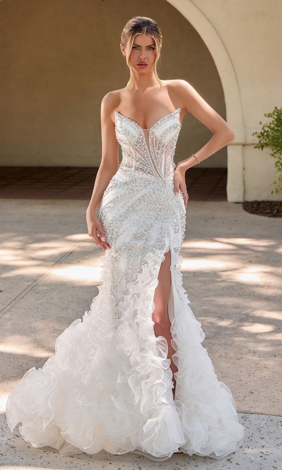 A woman stands outdoors on a sunny day wearing the Ladivine CC2488W, a stunning off white long formal dress featuring a strapless mermaid silhouette, intricate beadwork, high slit, and ruffled train—radiating elegance and style.